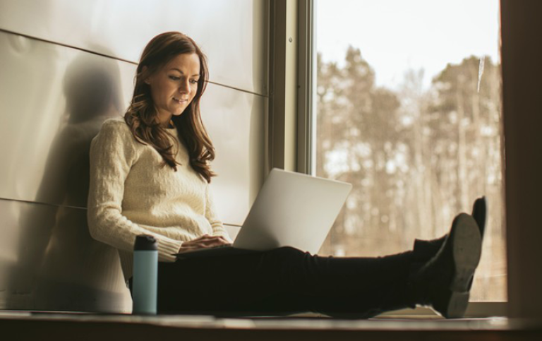Kvinnlig student sitter med dator i knät och jobbar.