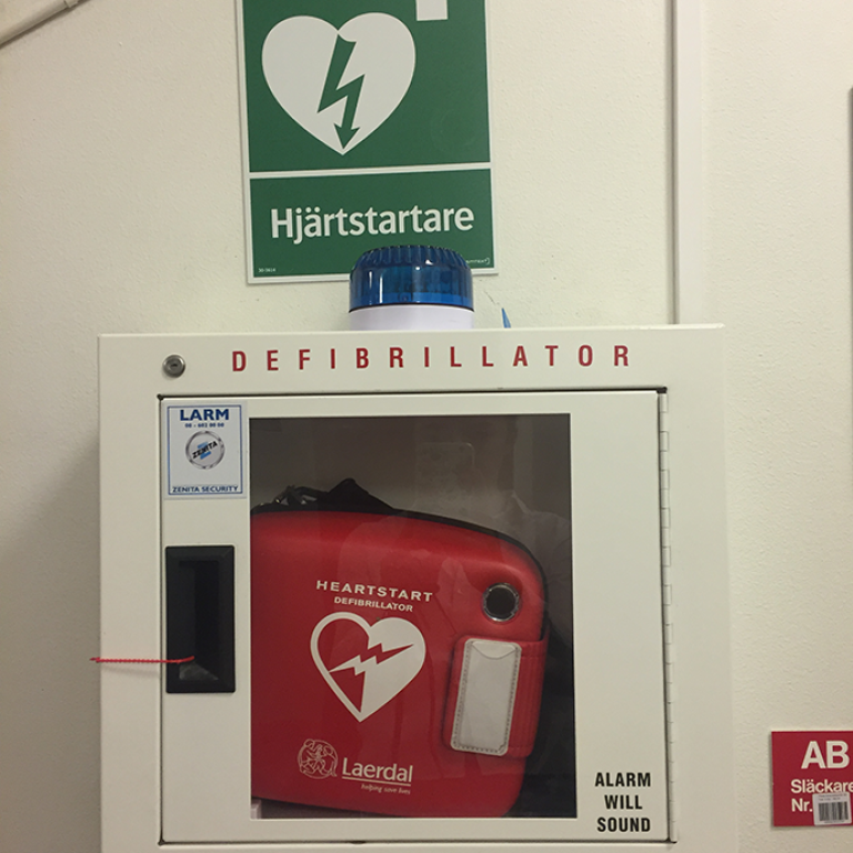 Defibrillator som hänger på en vit vägg.