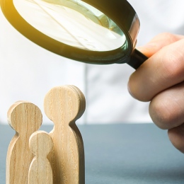 A man looks at wooden family figures under a magnifying glass.