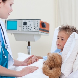 ett barn ligger i en sjukhussäng och blir undersökt av en doktor