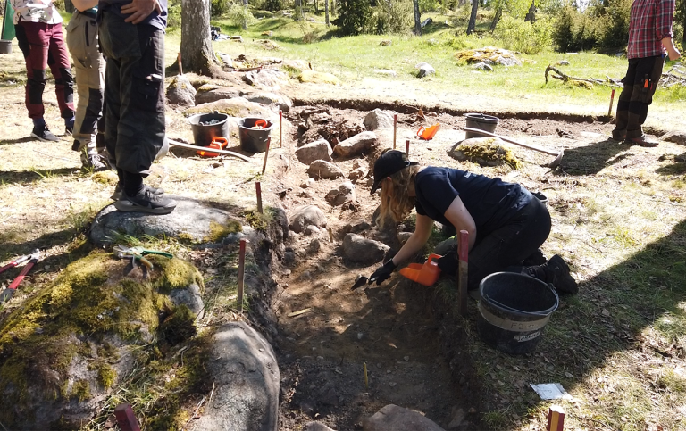 Utgrävningar på Birka våren 2022. vinklad grop i marken med arkeolger som gräver.