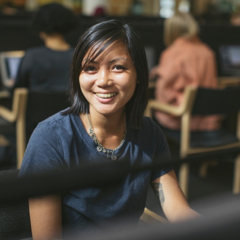 Student som sitter i universitetsbiblioteket och pluggar ler mot kameran. Foto: Niklas Björling