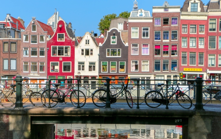 Colourful buildings reflected in water, and a bridge with parked bicycles