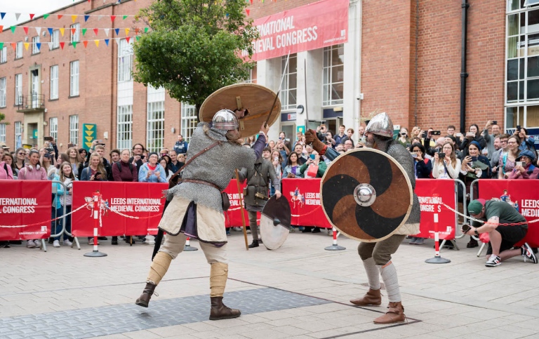 Två män i medeltida rustning slåss med svärd framför public