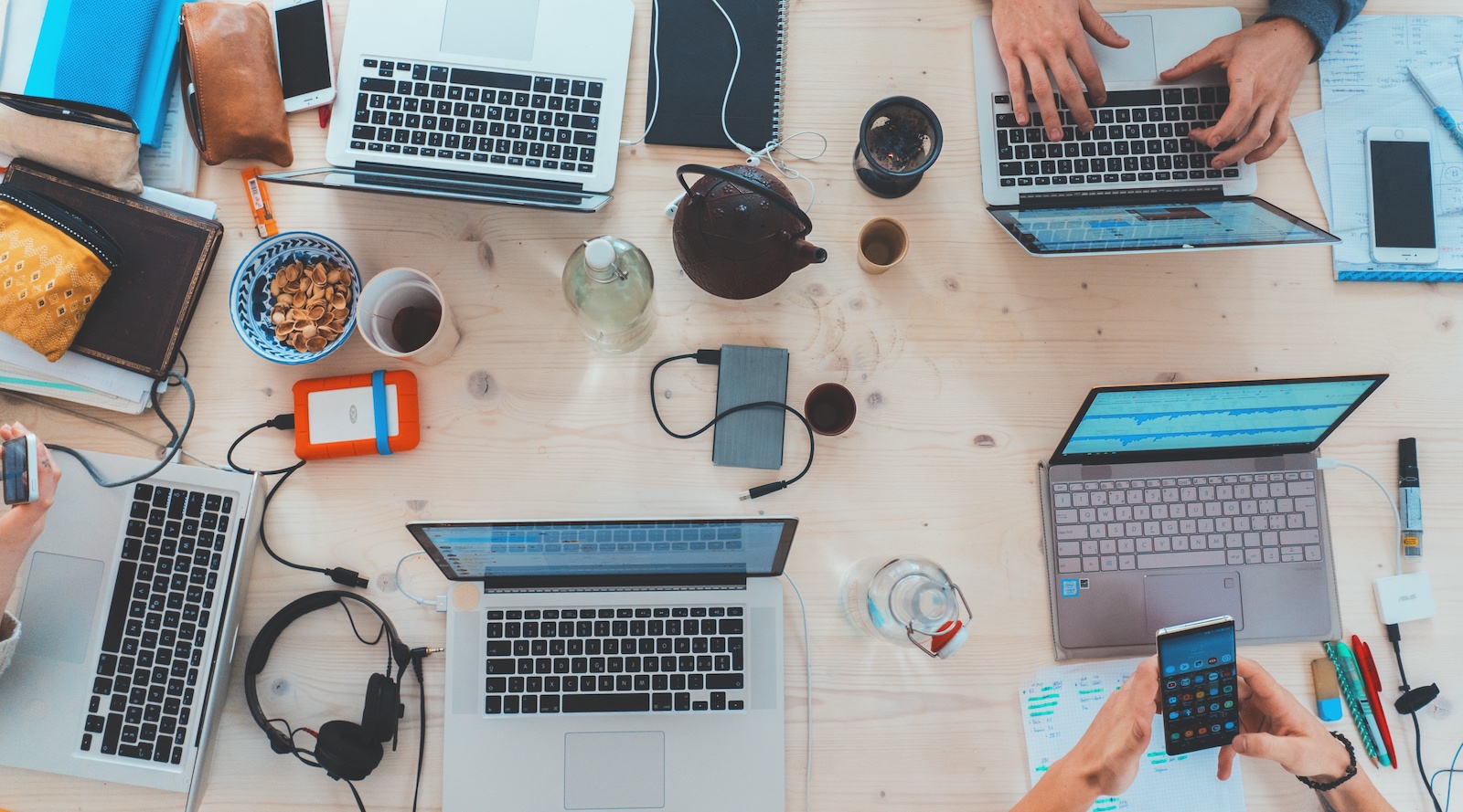 A desktop full of computers, accessories, coffee mugs etc.