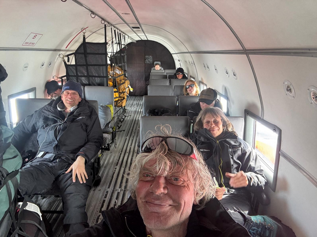 People flying on a small airplane. A man is in the front with sunglasses on his head, smiling.