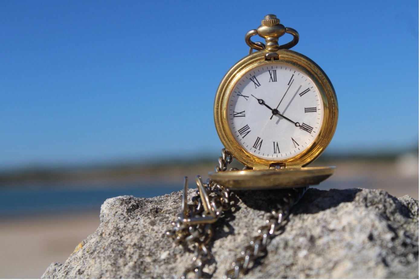 Old pocket watch on a rock near a lake.