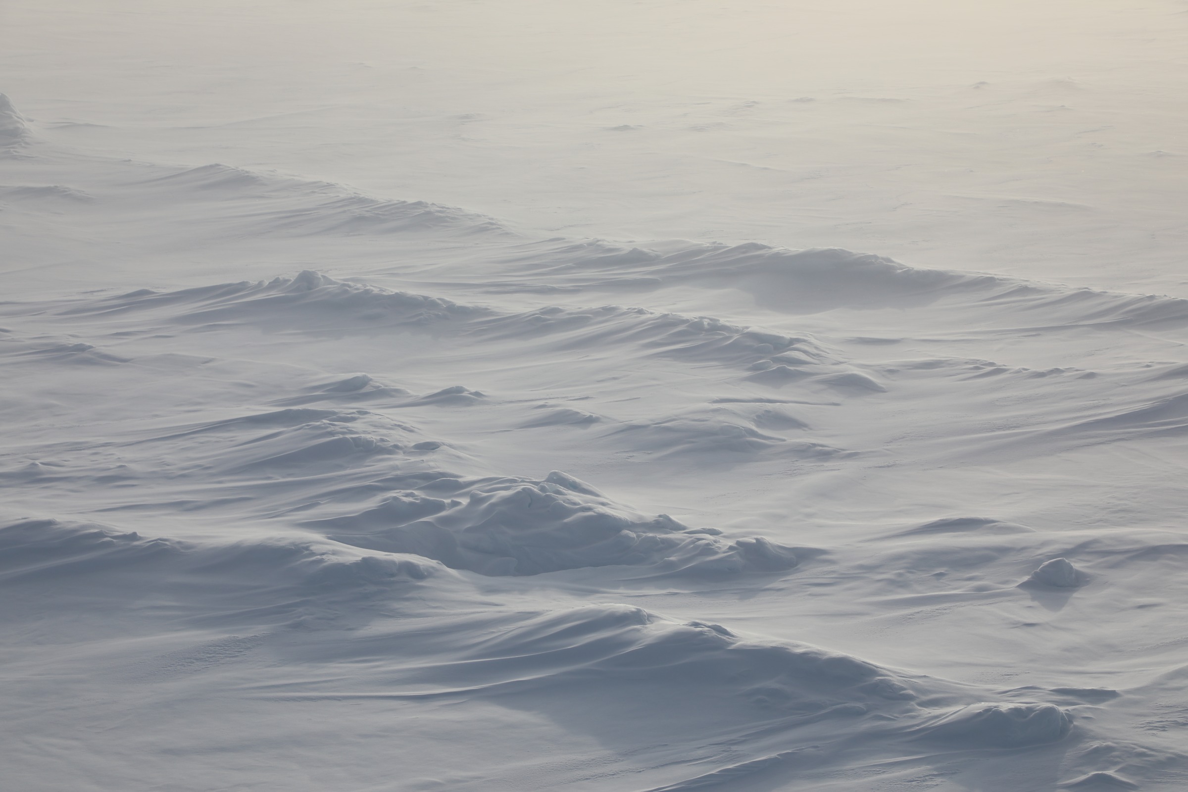 Snow accumulating around and blowing over sea ice ridges.