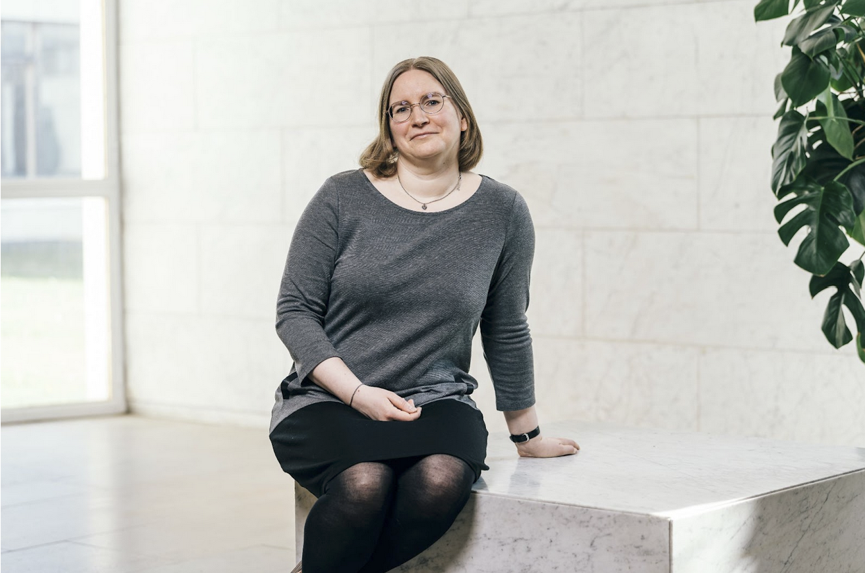 Woman sitting on a marble bench inside a building, smiling gently at the camera.