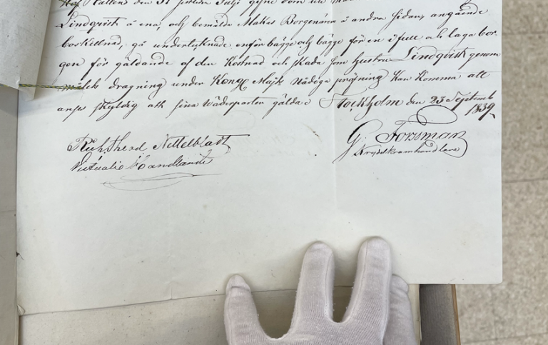 Foto av hand i vit hanske som håller i äldre handskrivet protokoll