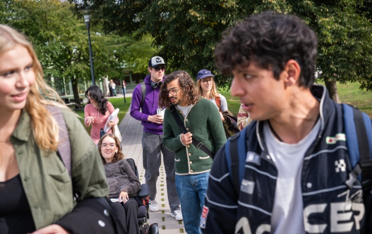 A bunch of students walking and wheeling outdoors, chatting.