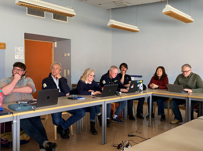 People seated around a U-shaped conference table during a meeting, facing inward and listening attentively