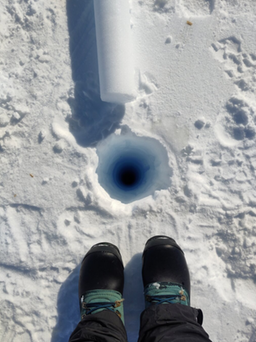 a drilled ice core hole that is blue down the middle with Ruth’s boots and part of the core visible. Image Credit Ruth Mottram