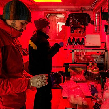 Två personer i labb med röd belysning.
