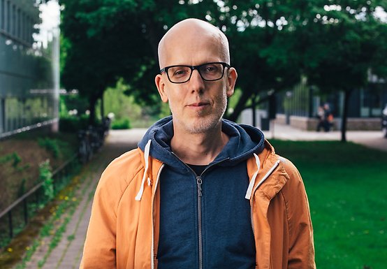 Jens Rydgren utomhus med grönska och campusbyggnad i bakgrunden.