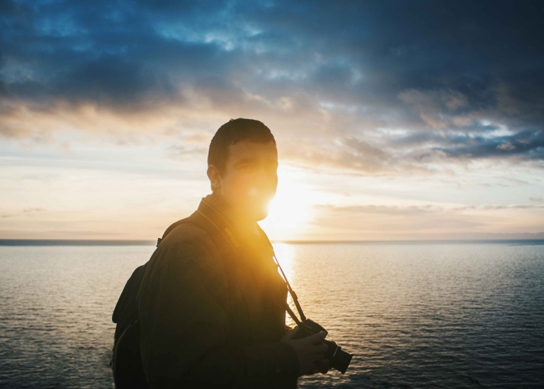 Kille med kamera vid havet i solnedgången