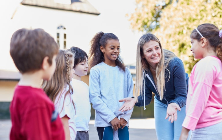 Gymnastiklärare pratar med en grupp gymnastikelever på skolgård. 