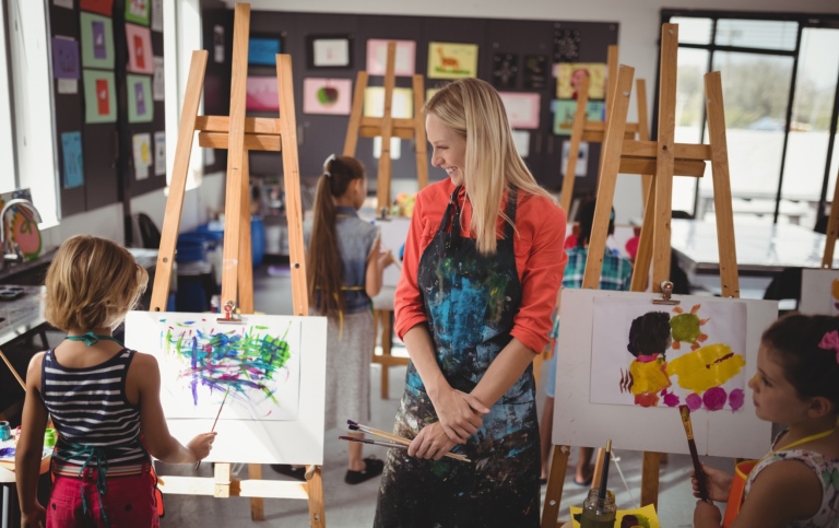 Bildlärare med elever som målar på stativ i klassrum