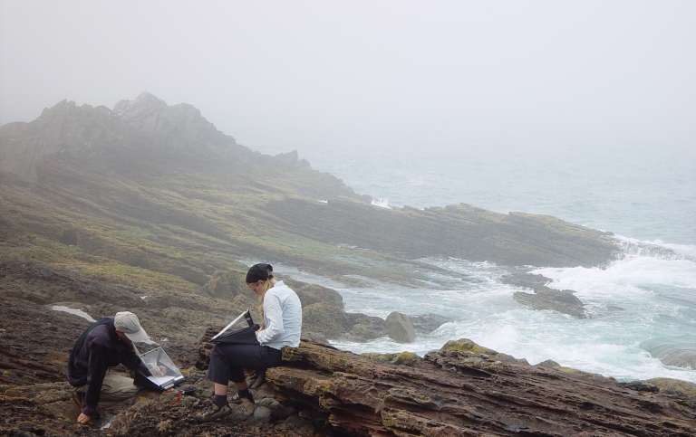 students sitting on a bedrock by the ocean writting notes