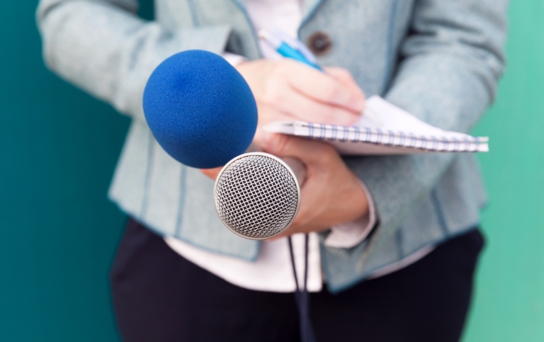 News reporter or TV journalist at press conference, holding microphone and writing notes
