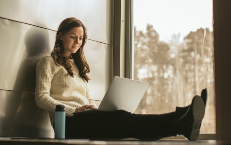 Tjej som sitter med bärbar dator i ett stort fönster. Foto: Niklas Björling