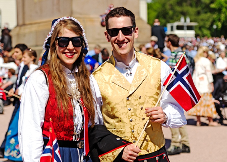 En ung kvinna och man i folkdräkt håller i norska flaggor på 17 maj i Oslo. Foto: Nataliia Anisimova