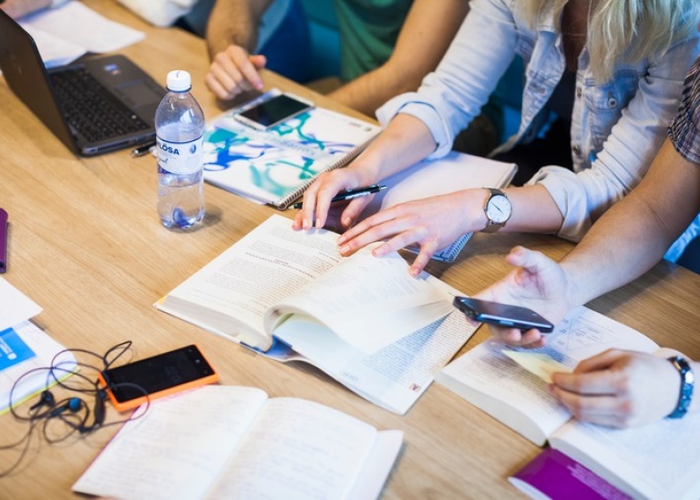 Studenter runt ett bord med böcker, papper, mobiler. Foto: Niklas Björling