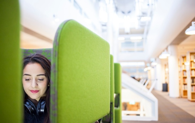 Woman with headphones in a green armchair in the library. Photo: Niklas Björling