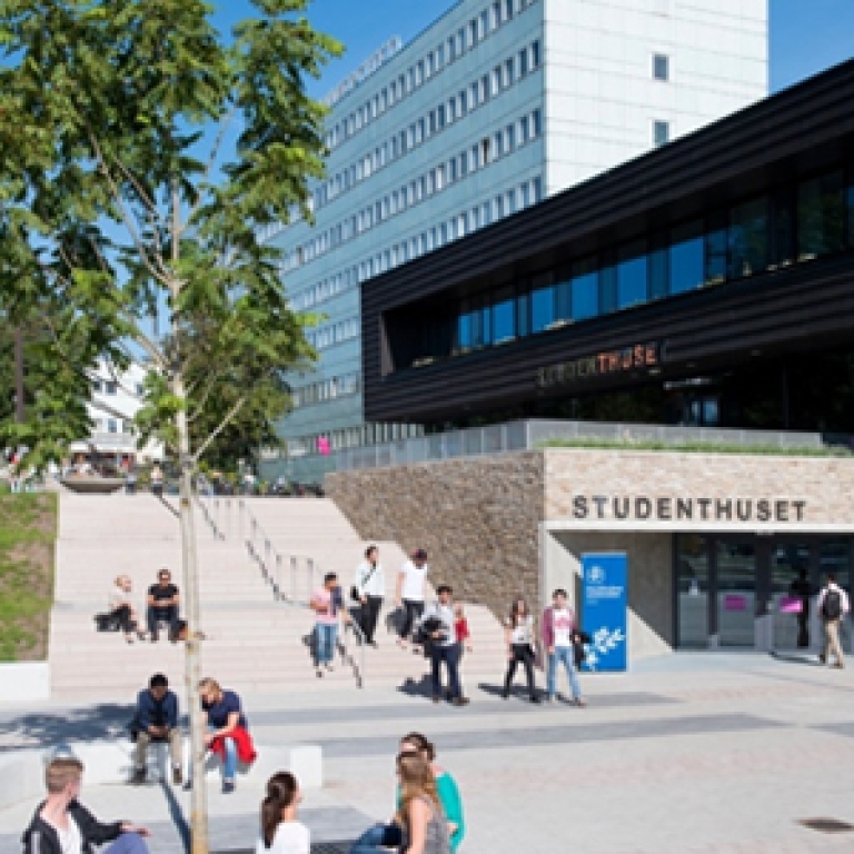 a view of the student house at Stockholm University, with students walking by and sitting outside