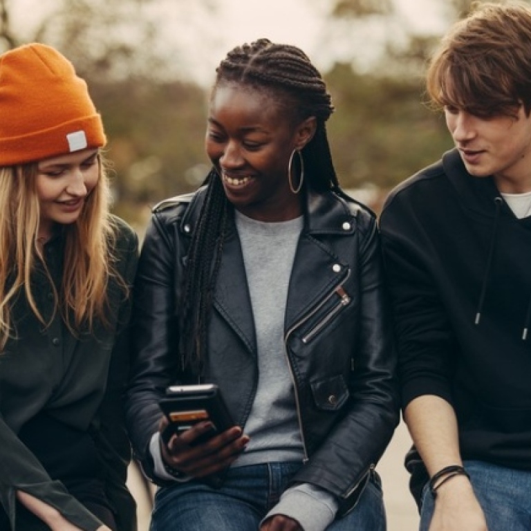 three students sitting and looking at a cell phone