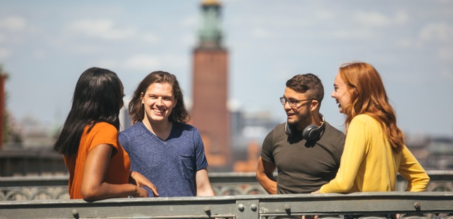 Fyra unga personer står på en bro med Stadshuset i bakgrunden