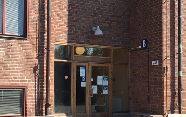 Frescativägen 24F. Foto: Stockholms universitet Glasdörr i en brun tegelbyggnad.