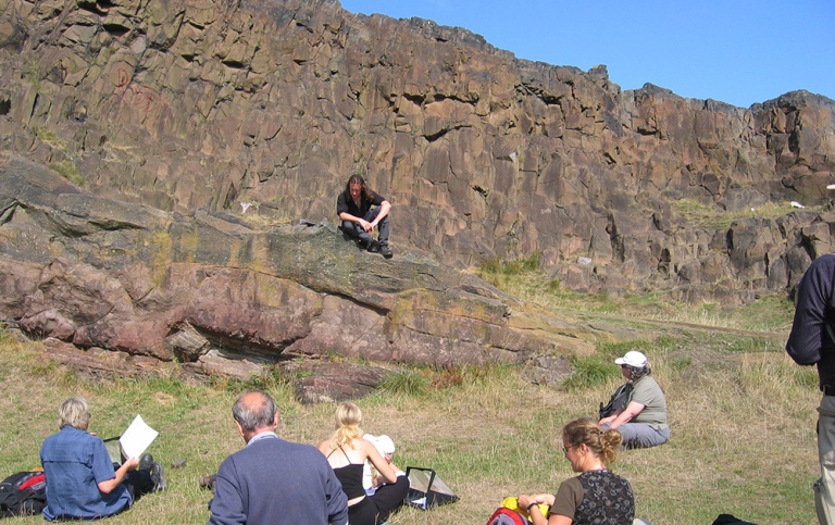 teacher sitting on top of rocks, students sittng around, scotland
