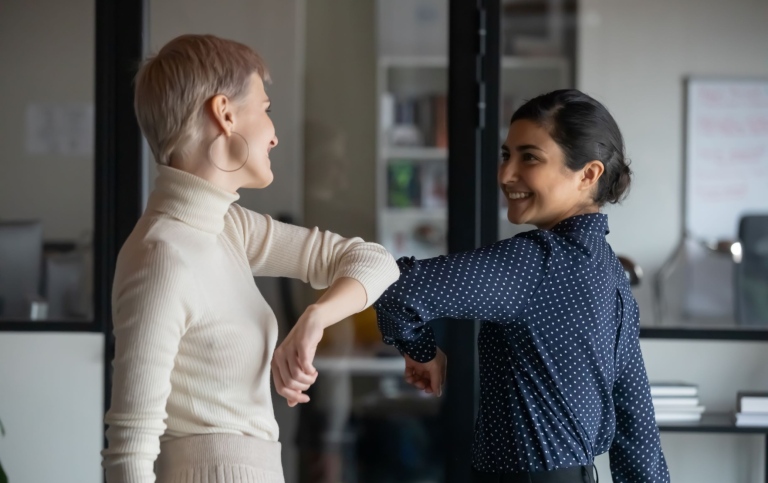 Två glada kvinnliga studenter gör coronahälsning med armbågarna. Foto från Shutterstock