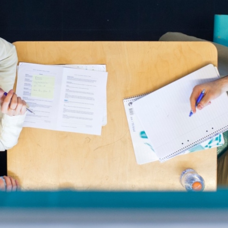 Två studenter sitter vid ett bord och pluggar, sedda ovanifrån
