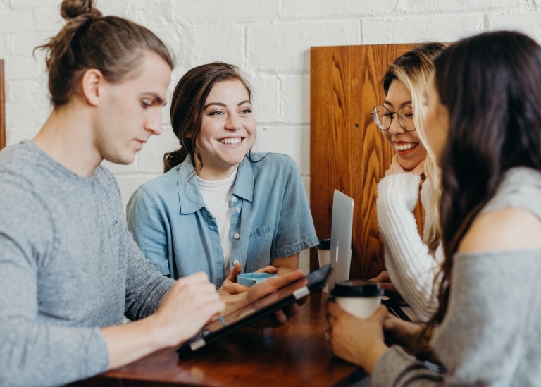 Fyra personer står och pratar vid ett café-bord. Photo by Brooke Cagle on Unsplash.