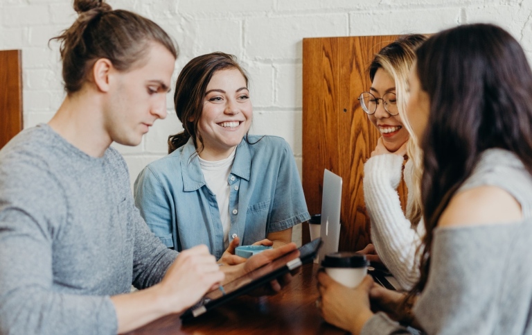 Fyra personer står och pratar vid ett café-bord. Photo by Brooke Cagle on Unsplash.