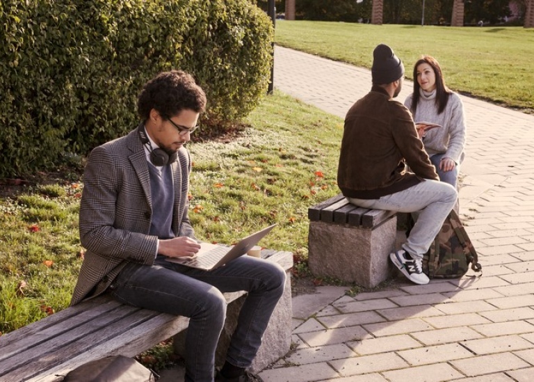 Three students on campus, one has a laptop.