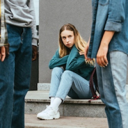 En flicka i högstadieåldern sitter på en trappa och tittar bort mot ett par vänner