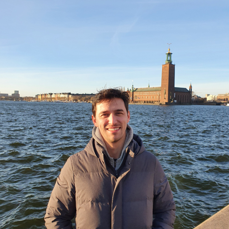 A photo of Guilherme Tácito de Luna in front of lake Mälaren and the Stockholm City Hall