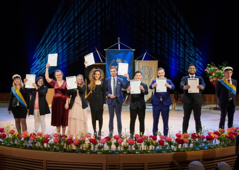 Examinerad masterstudenter står på scen och visar upp sina diplom. Foto: Ingmarie Andersson.