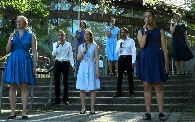 Women and men sing in summer clothes outside Aula Magna