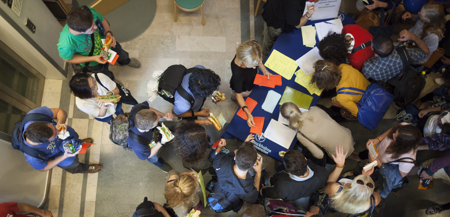 Många studenter sedda uppifrån, kring ett bord med papper och broschyrer.