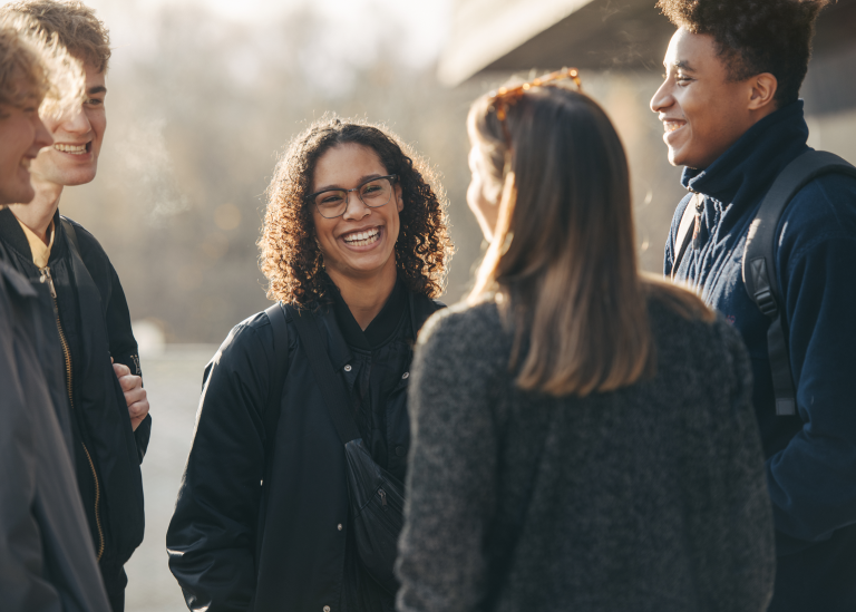 Five students standing, talkning and laughing.