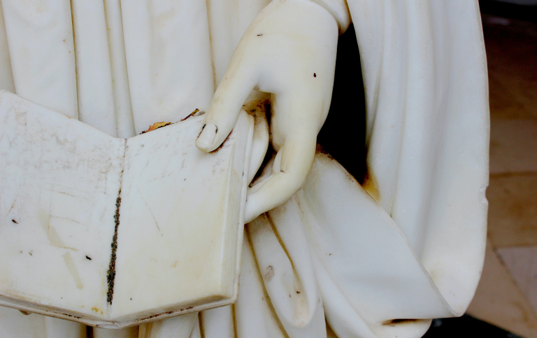 Detail of marble statue, hand holding an open book. Photo: Unsplash