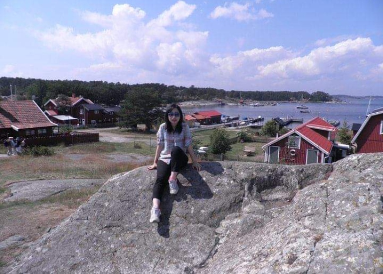 Bonjung Goo sitting on a rock in with water and red houses in the background