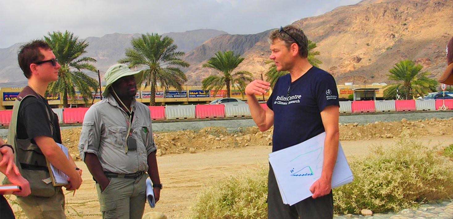 Teacher talking to students on fieldwork, desert landscape, with palm trees on the background.