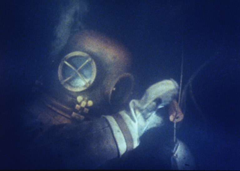 En dykare i gammaldags dykardräkt under havet.