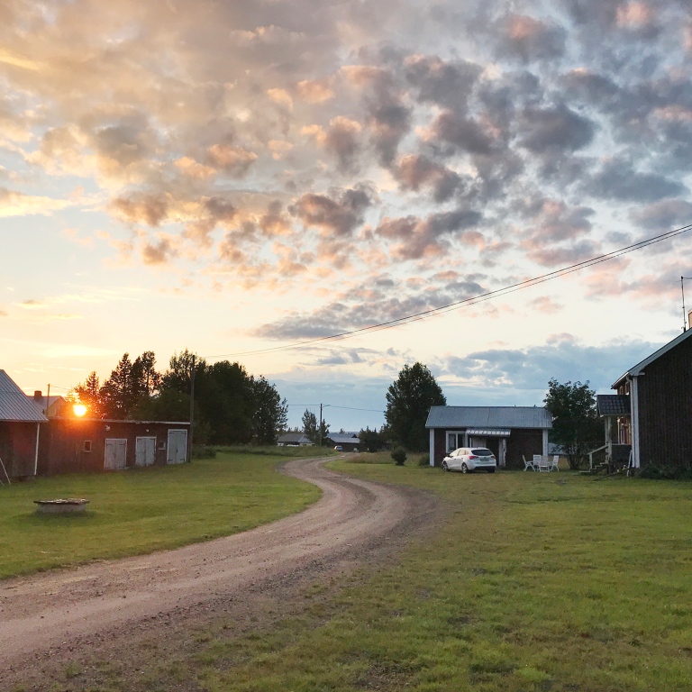 gårdsplan med ladugård och rött bostadshus i solnedgång