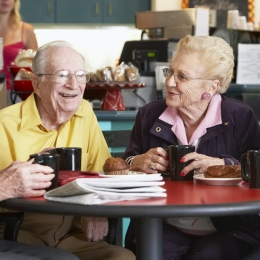 Äldre personer runt ett bord fikar och skrattar